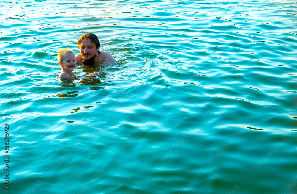 The little boy in his father's arms, in the waves of the sea. Dad with the little child on vacation.