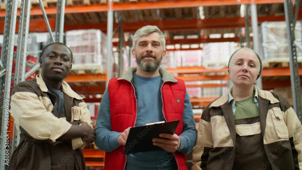 Group portrait of middle aged manager and diverse technicians standing in warehouse and posing together for camera Group portrait of middle aged manager and diverse technicians standing in warehouse and posing together for camera
