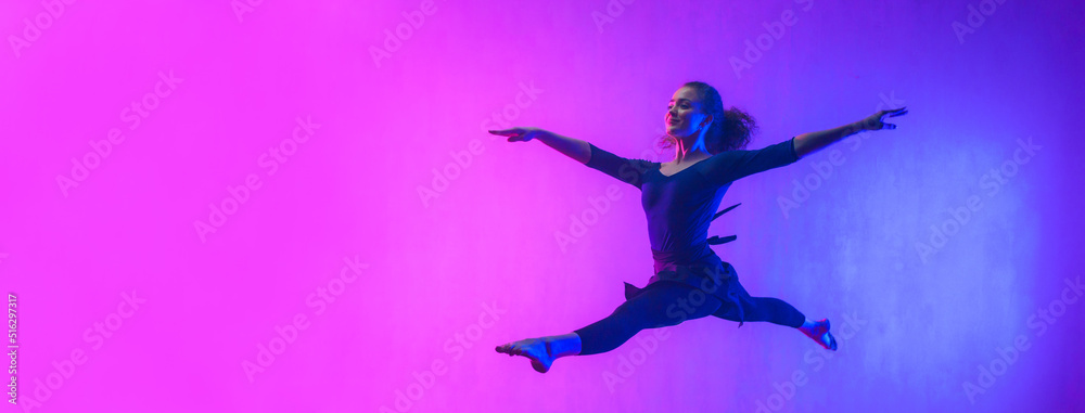 Modern dance girl dancer jumping up dancing in neon light doing gymnastic exercises in studio, wide banner, copy space. Modern dance girl dancer jumping up dancing in neon light doing gymnastic exercises in studio, wide banner, copy space.