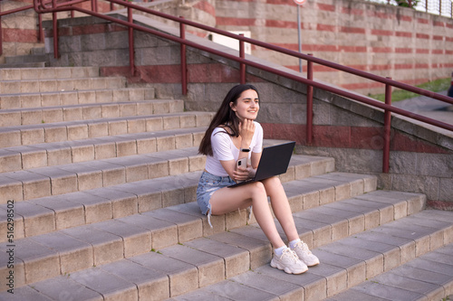 the girl is sitting on the stairs, laptop on her lap, looking into the distance