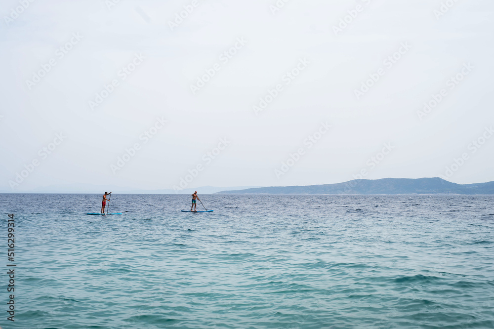 Men spending leisure time while enjoying paddling on SUP in sea during summer. Summer vacation concept.