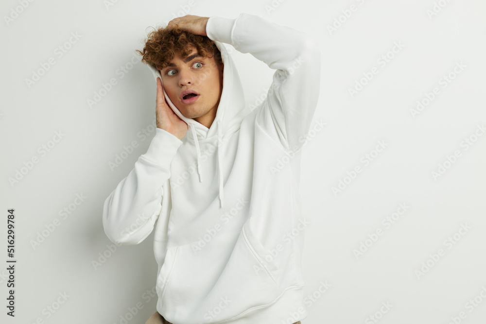 a cute man stands on a white background in a white hoodie on his head and holds his hand near his face, making a funny expression with his mouth wide open a cute man stands on a white background in a white hoodie on his head and holds his hand near his face, making a funny expression with his mouth wide open