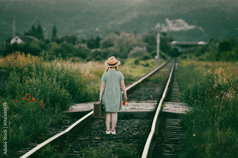 A little girl in a dress walking on an abandoned railroad tracks