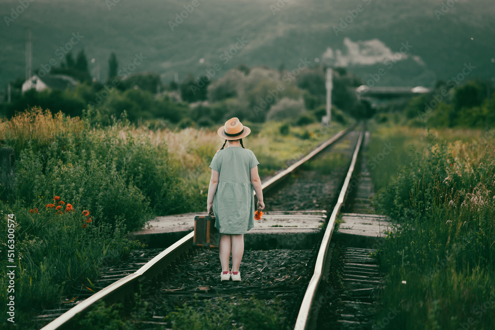 Fototapeta premium A little girl in a dress walking on an abandoned railroad tracks