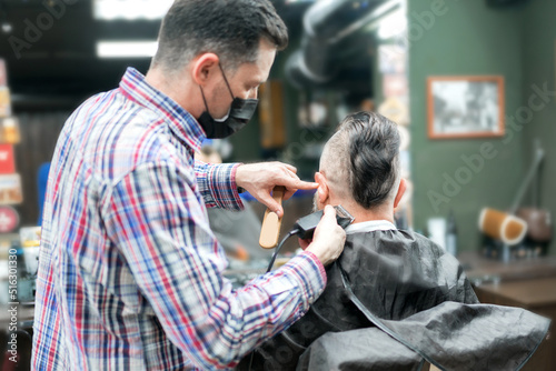 An adult man with a mohawk in a barbershop. The master