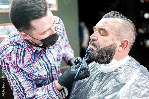 Quadro su tela Beard dyeing in a barbershop. a young master applies paint