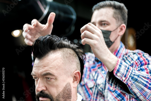 An adult man in a barbershop with a beard and a mohawk.