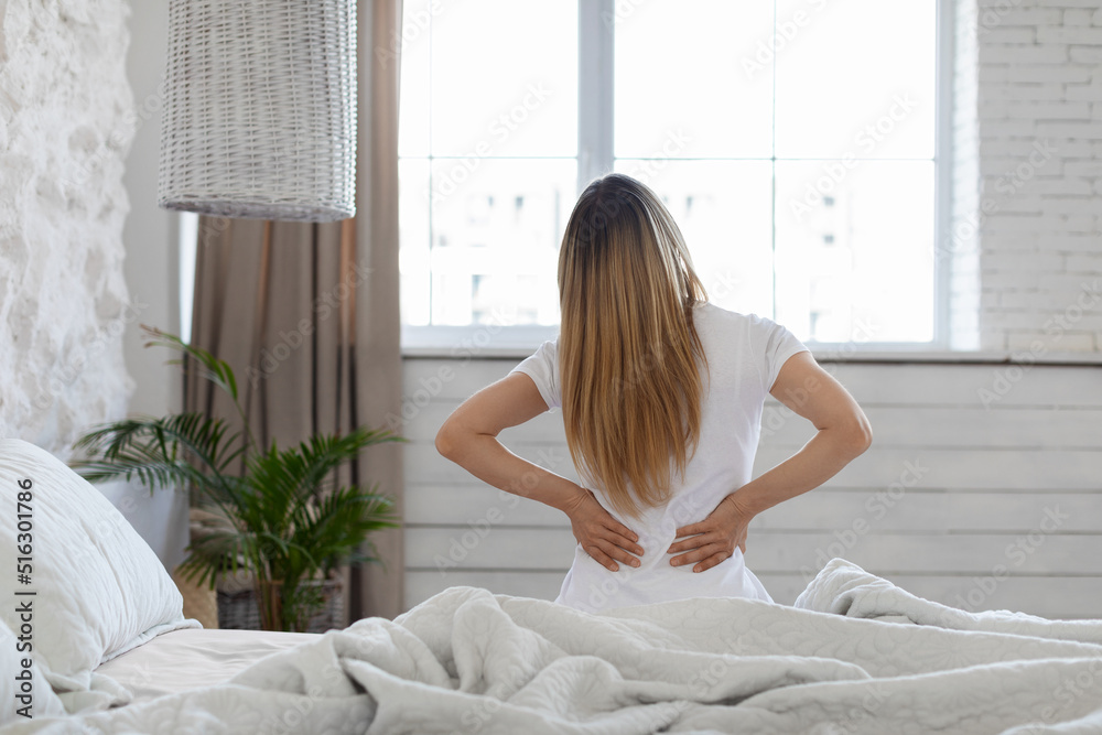 Unrecognizable woman suffering from back pain at home in bedroom Unrecognizable woman suffering from back pain at home in bedroom