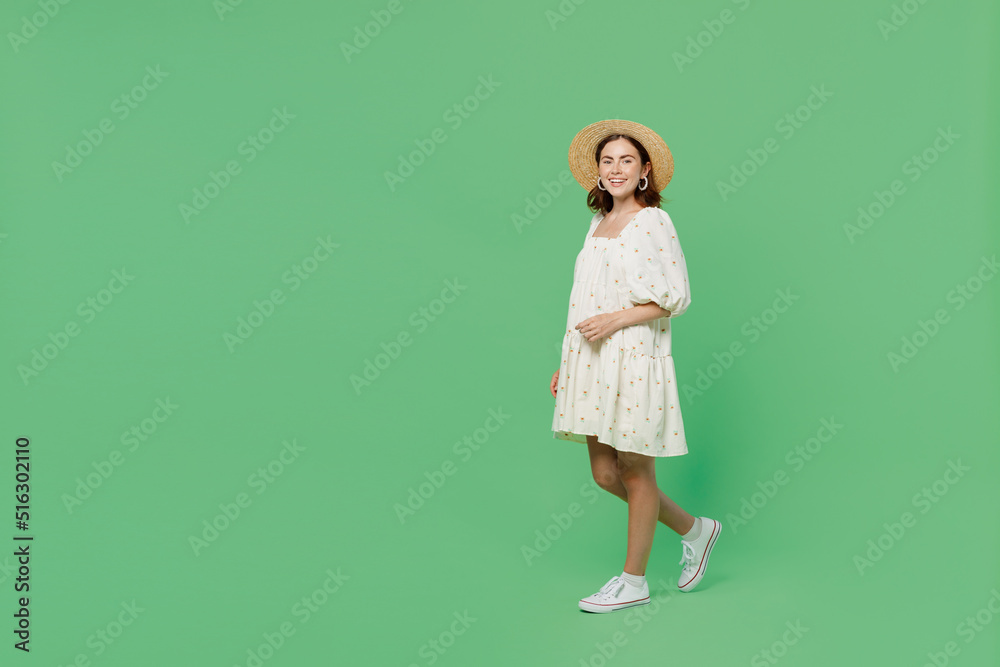 Full body side view young happy smiling fun cheerful woman she 20s in white dress hat walking go look camera isolated on plain pastel light green background studio portrait. People lifestyle concept Full body side view young happy smiling fun cheerful woman she 20s in white dress hat walking go look camera isolated on plain pastel light green background studio portrait. People lifestyle concept
