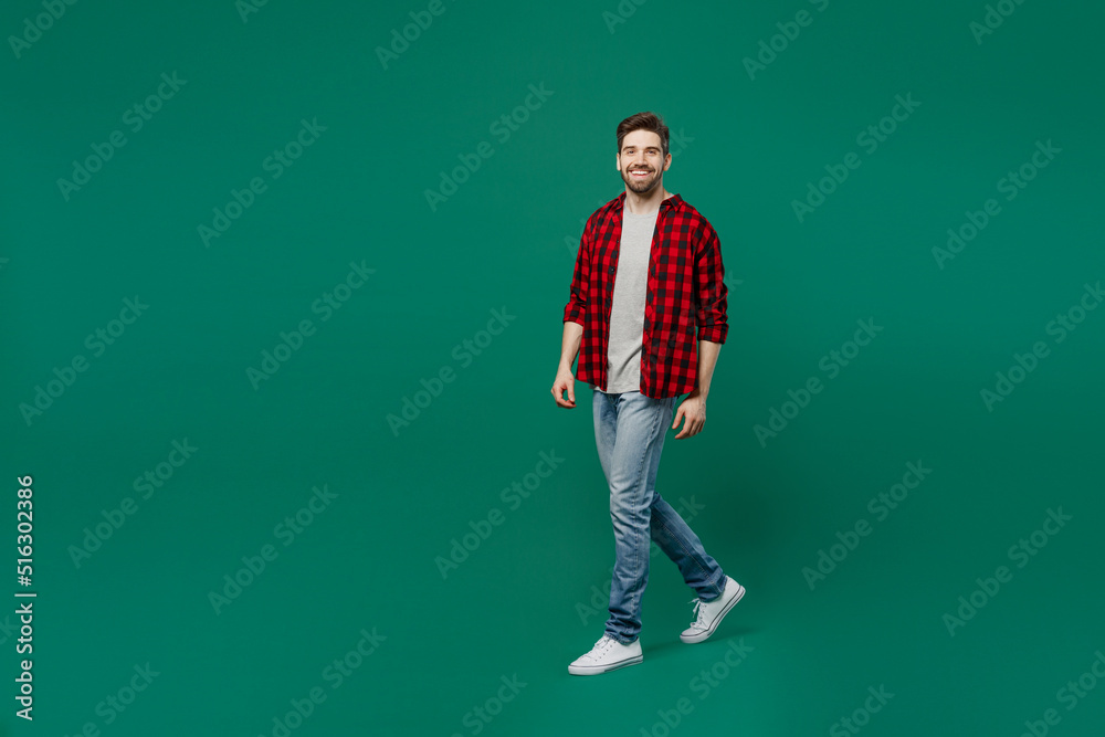 Full body young happy smiling caucasian man he 20s wearing red shirt grey t-shirt walking going strolling look camera isolated on plain dark green background studio portrait. People lifestyle concept. Full body young happy smiling caucasian man he 20s wearing red shirt grey t-shirt walking going strolling look camera isolated on plain dark green background studio portrait. People lifestyle concept.