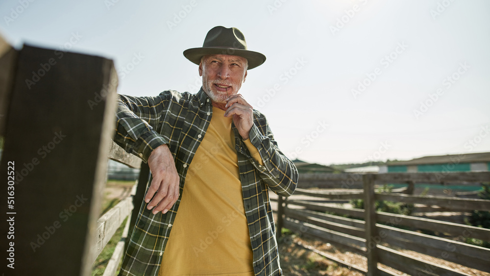 Senior male farmer looking away at fence on farm Senior male farmer looking away at fence on farm