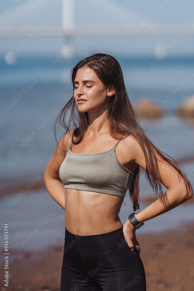 Attractive young Spanish woman standing outdoors in sport bra and pants  looking at camera smiling Stock Photo by ionadidishvili