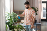 people, nature and plants care concept - man spraying houseplant by water sprayer at home