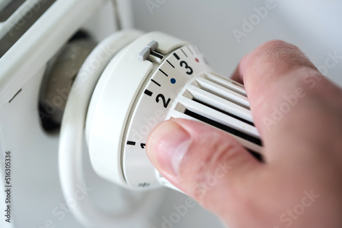 person adjusting thermostat on radiator to lower temperature, saving energy and money concept photo