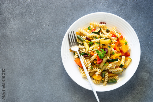 Vegan pasta fusilli with vegetables, zucchini, paprika and grean beans. Top view on stone table.