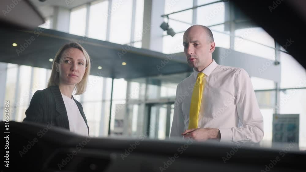 Attractive woman picks up her car in a car dealership. Friendly seller, advises the client.