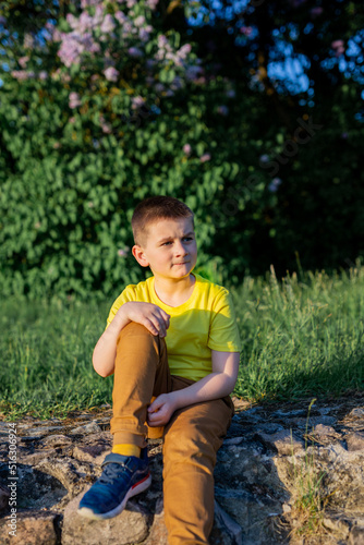 schoolboy boy in a yellow T-shirt sits outdoors