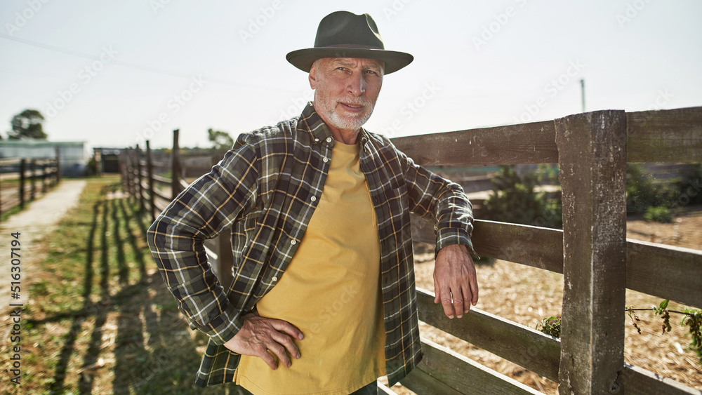 Elderly male farmer looking away at fence on farm Elderly male farmer looking away at fence on farm