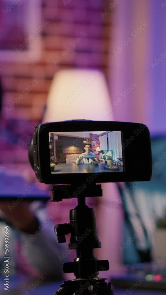 Vertical video: Camera on tripod filming podcast show with man doing product review of laptop, social media content. Live broadcasting video with wireless computer recommendation on online channel. Vertical video: Camera on tripod filming podcast show with man doing product review of laptop, social media content. Live broadcasting video with wireless computer recommendation on online channel.