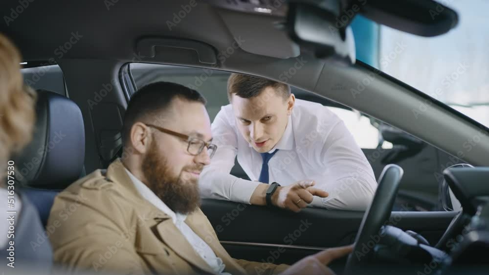 A married couple in a large car dealership. The couple sits in the car, the manager talks about the technical equipment of the car. A married couple in a large car dealership. The couple sits in the car, the manager talks about the technical equipment of the car.