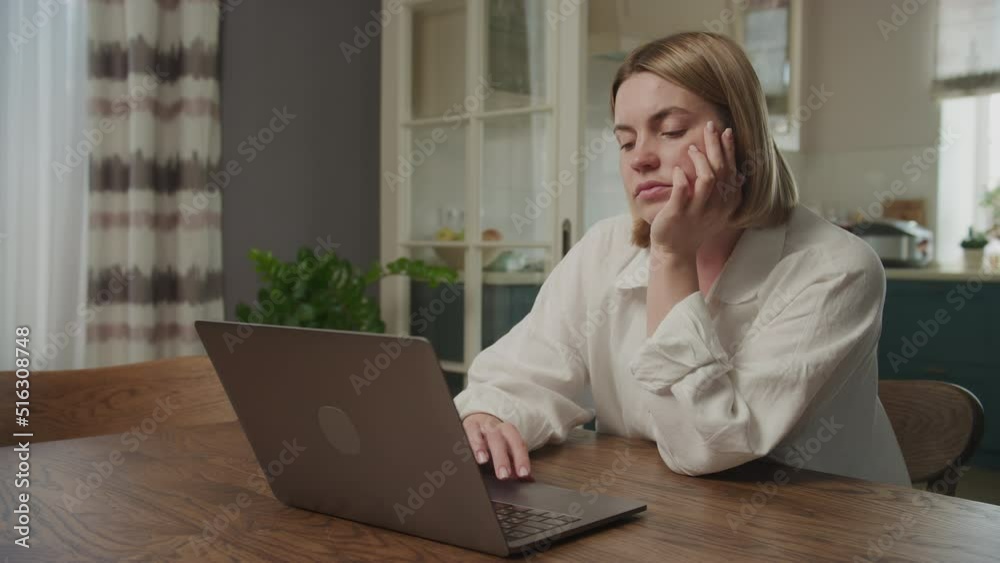 Caucasian woman browsing bored on her laptop computer in her apartment Caucasian woman browsing bored on her laptop computer in her apartment