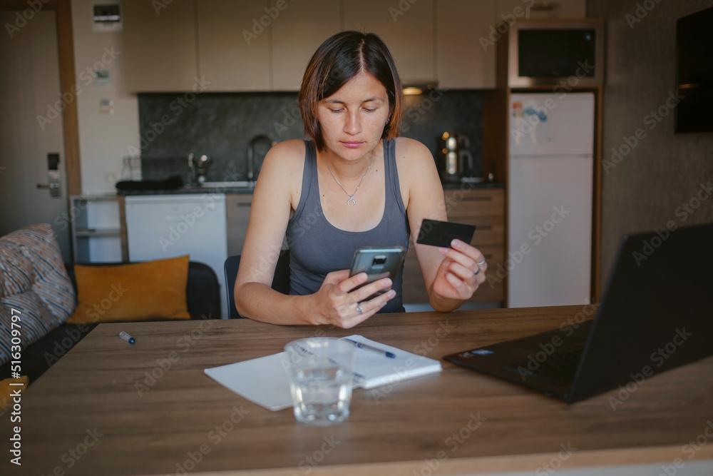 young asian woman at home, remote work at laptop. shopping online at home, lady is holding credit card and using smartphone and computer.