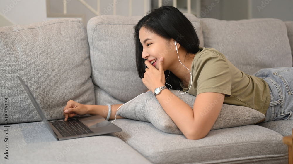 Relaxed asian woman lying on couch and surfing internet on laptop computer Relaxed asian woman lying on couch and surfing internet on laptop computer