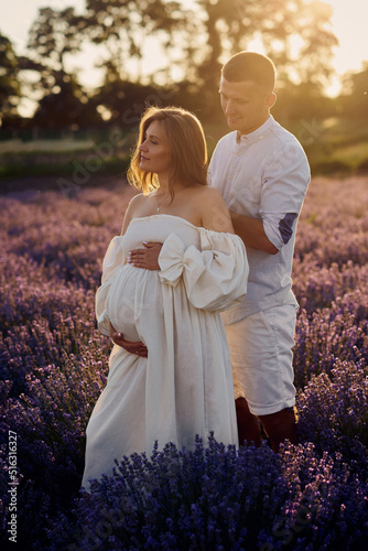 portrait of a young beautiful pregnant couple on a lavender field at sunset. Happy family concept