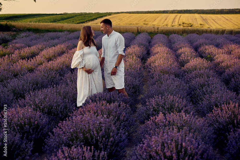 young beautiful pregnant couple walking on a lavender field at sunset. Happy family concept