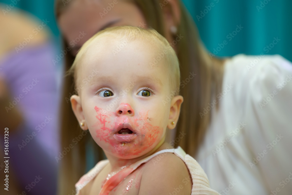 The little girl smeared her face with pink sweet cream. The little girl smeared her face with pink sweet cream.