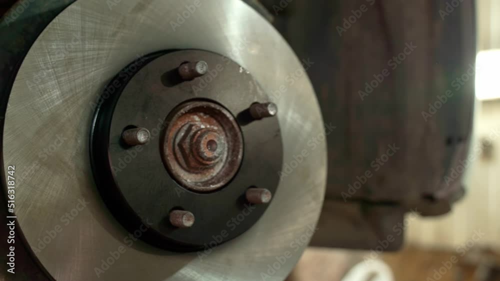 auto mechanic replaces the brake disc of a car wheel of a lifted car at a repair station. Hands of an auto mechanic in gloves close-up. auto mechanic replaces the brake disc of a car wheel of a lifted car at a repair station. Hands of an auto mechanic in gloves close-up.