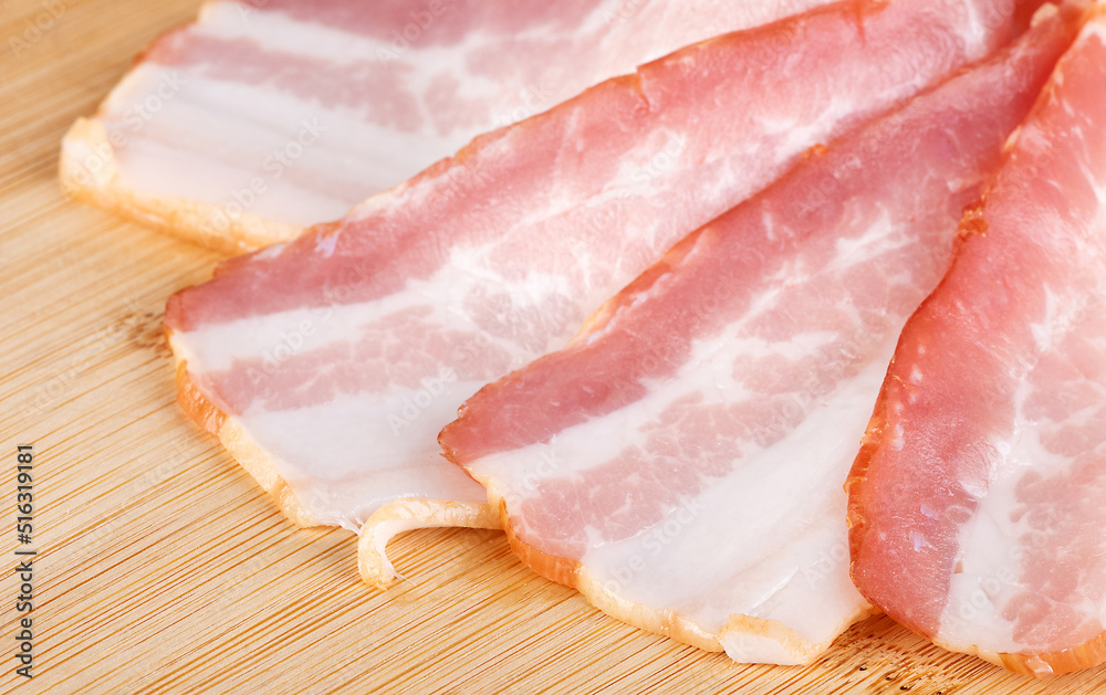 slices of raw bacon on a cutting board with basil, isolated on a white background