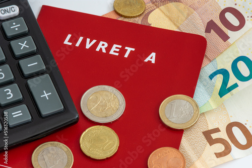 Livret A avec pièces et billets en euros et une calculette. Le livret A est un compte épargne français règlementé dont le taux d'intérêt et le plafond de dépôt sont définis par le gouvernement