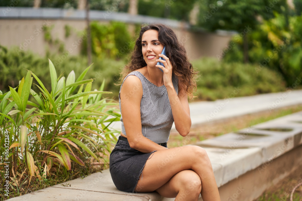 Naklejka premium happy young girl talking on mobile phone sitting in park