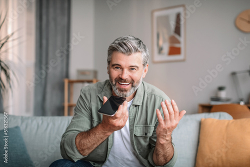 Glad happy emotional caucasian mature male with beard speaks by phone in living room interior