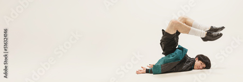 Fotomural Portrait of stylish young man in black outfit and green coat lying on floor isolated over grey studio background
