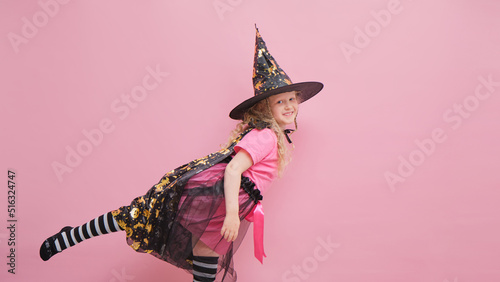 cute cheerful girl 6 years old in a witch costume on a pink background