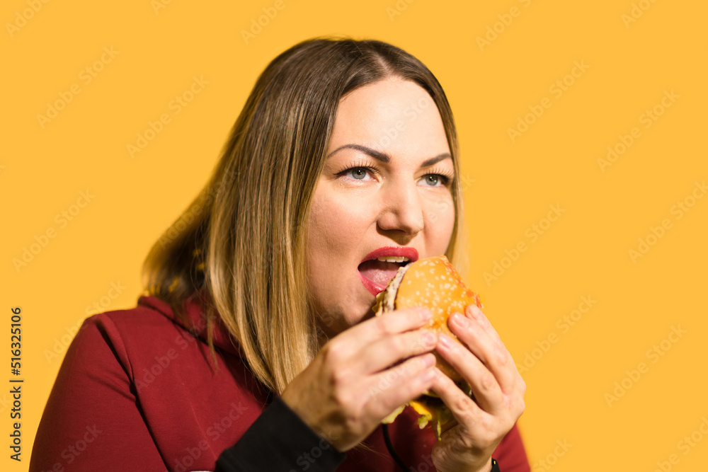 A hungry woman is biting a big tasty burger