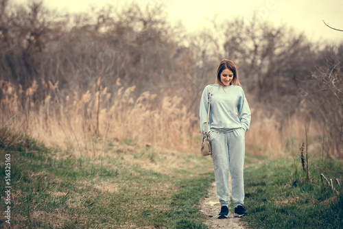 a slender girl in a tracksuit walks along the path of the park in early spring