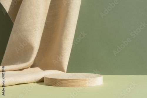 Wooden cylindrical podium, pedestal on a green background with beige curtain. Scene for the presentation of a cosmetic product. Empty showcase