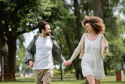 happy couple in summer clothes holding hands in green park.