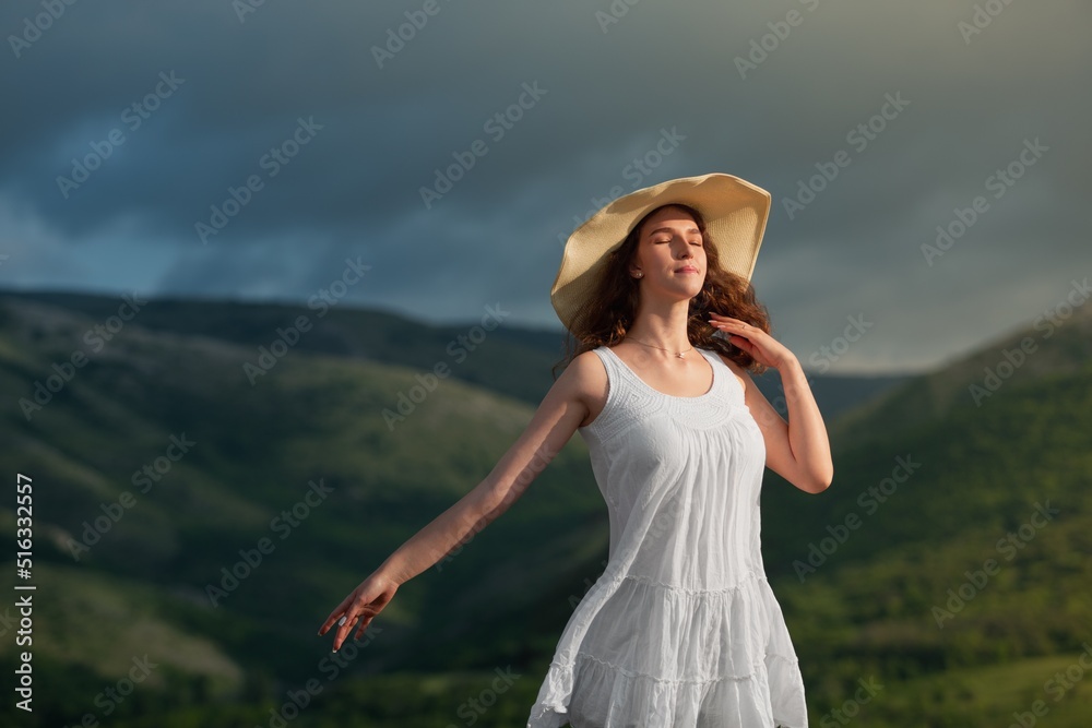 Woman in a hat on the field with flowers on the landscape background