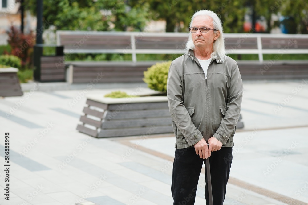 Portrait of senior man holding walking stick while resting in park. Portrait of senior man holding walking stick while resting in park.