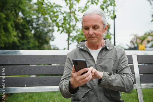Old man browsing app on smartphone, outdoor in park