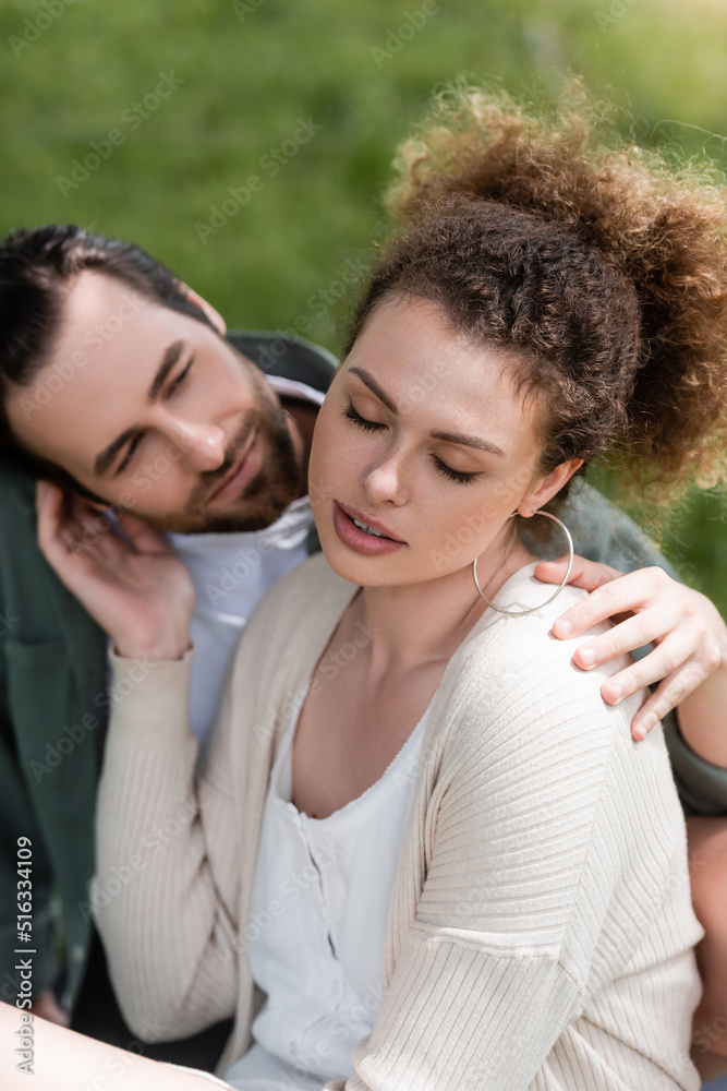 tender and curly woman touching face of bearded boyfriend in park. tender and curly woman touching face of bearded boyfriend in park.