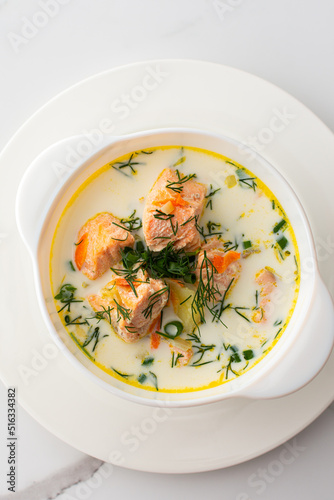 Norwegian red salmon fish soup with vegetables, herbs and cream, top view of a bowl of soup on a white marble background