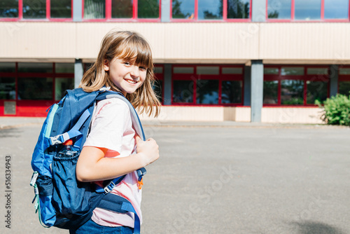 Portrait of a happy schoolgirl girl with a backpack on her back against the school. Children go to school. Beginning or end of lessons and school year