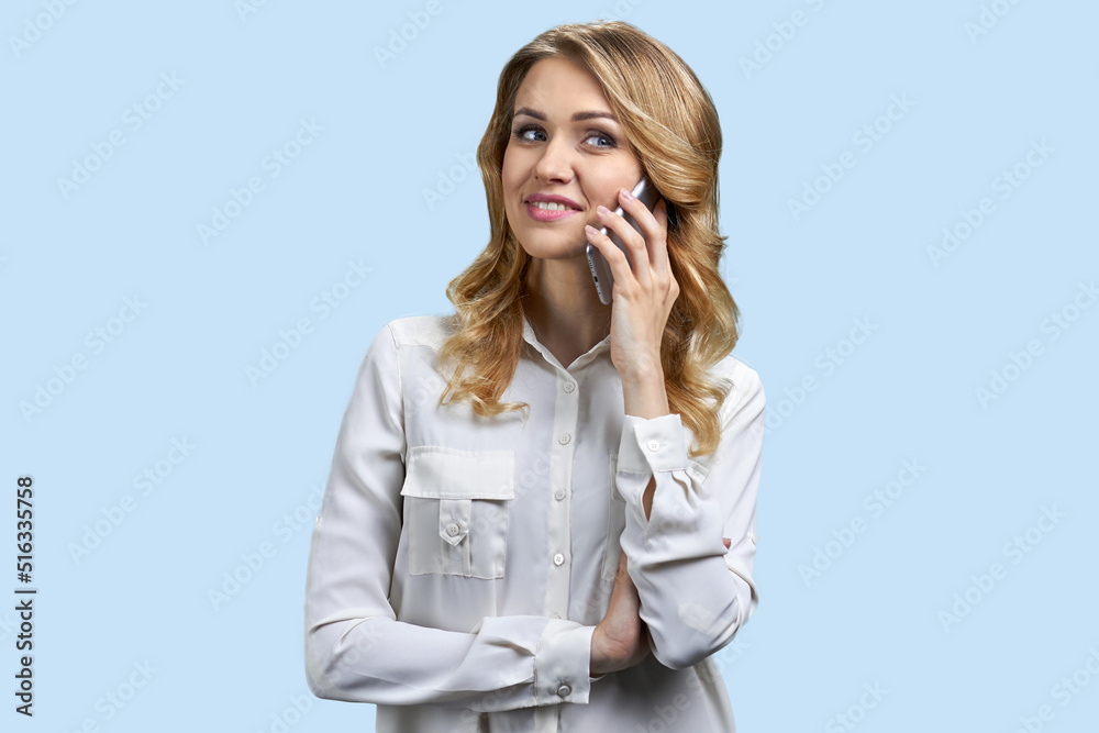 Attractive young woman talking on mobile phone and smiling. Pretty woman talks on cell phone on blue background. Attractive young woman talking on mobile phone and smiling. Pretty woman talks on cell phone on blue background.