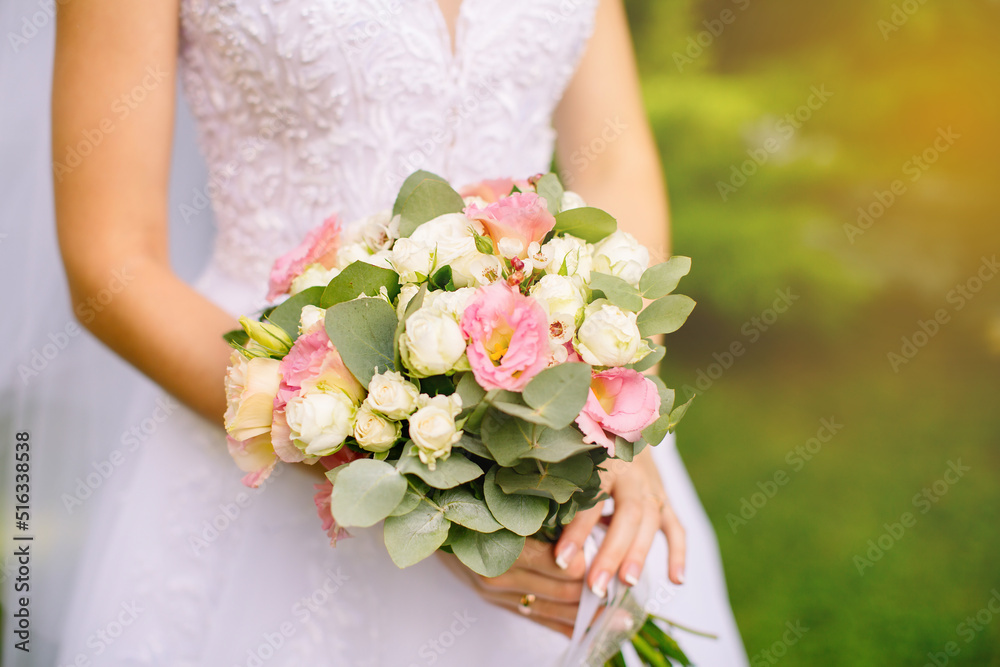 Bride with a wedding bouquet in her hands is in the summer garden, the wedding floristry of white and pink roses. High quality shot Bride with a wedding bouquet in her hands is in the summer garden, the wedding floristry of white and pink roses. High quality shot
