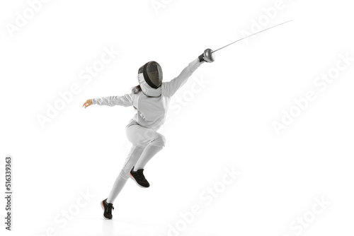 Young girl, beginner fencer in fencing costume and mask practicing with rapier isolated on white background. Sport, youth, healthy lifestyle, achievements.